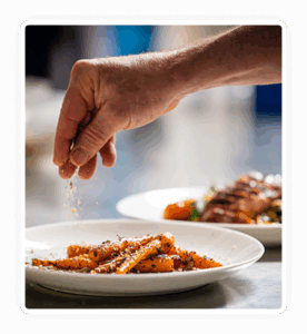 Hand sprinkling salt on cooked ribs on a white plate.